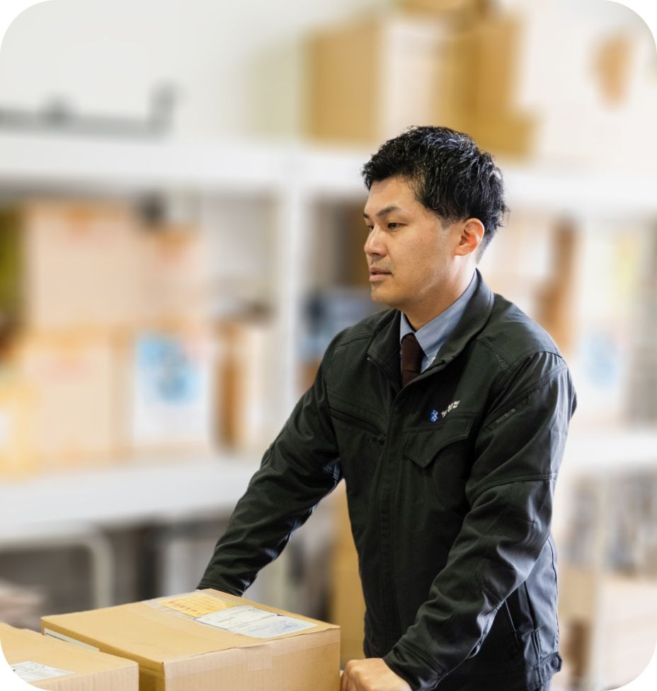 倉庫で段ボール箱を手に取り出荷準備をするサンワ包装の男性営業社員