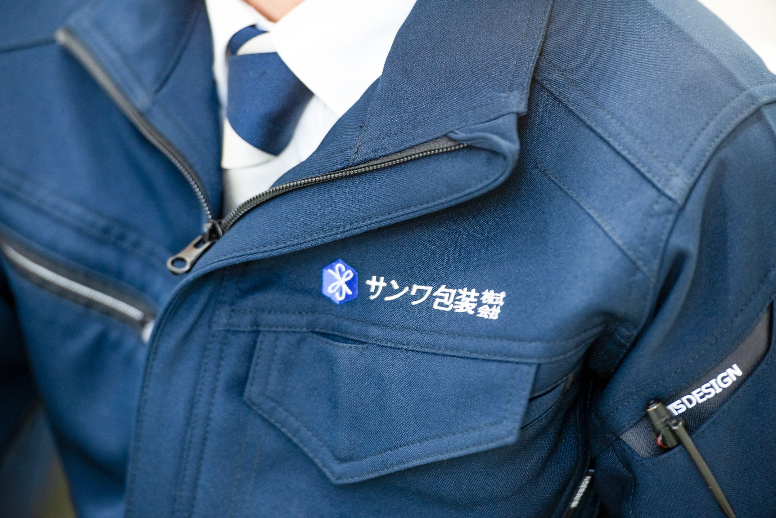 サンワ包装のロゴが胸元に刺繍された紺色の作業着を着る社員